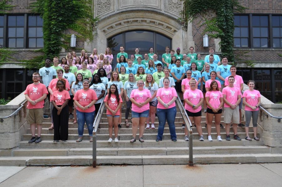 New RAs stand outside of Somsen Hall during their training week, their shirts display the new WISE logo which represents Housings mission statement of being welcoming, inclusive, safe and engaging and each building staff received a different color.